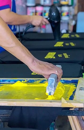 Siebdruck gelbe Farbe wird mit Rakel auf schwarze Shirts gedruckt