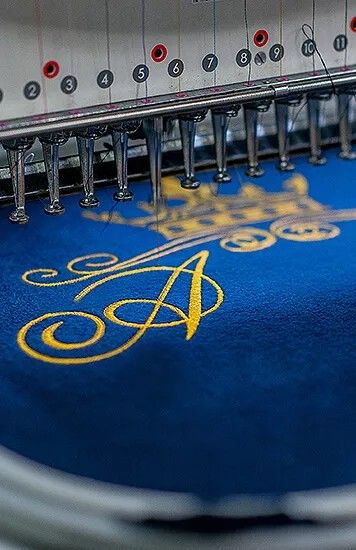 Stickmaschine stickt goldenes Monogramm auf blauem Stoff